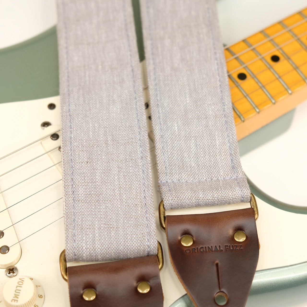 Wide view of guitar strap in cool light grey shimmery woven fabric with brown leather end-tab. Made in Nashville by Original Fuzz.