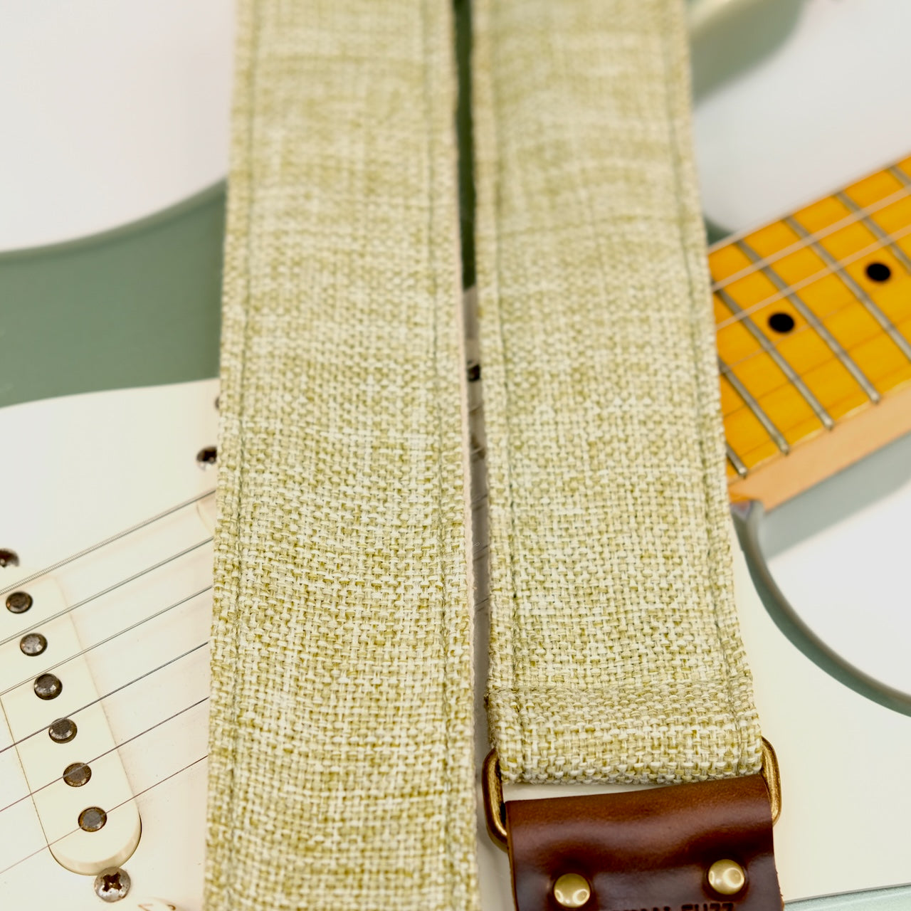 Wide view of guitar strap in green and cream woven fabric with brown leather end-tab. Made in Nashville by Original Fuzz.