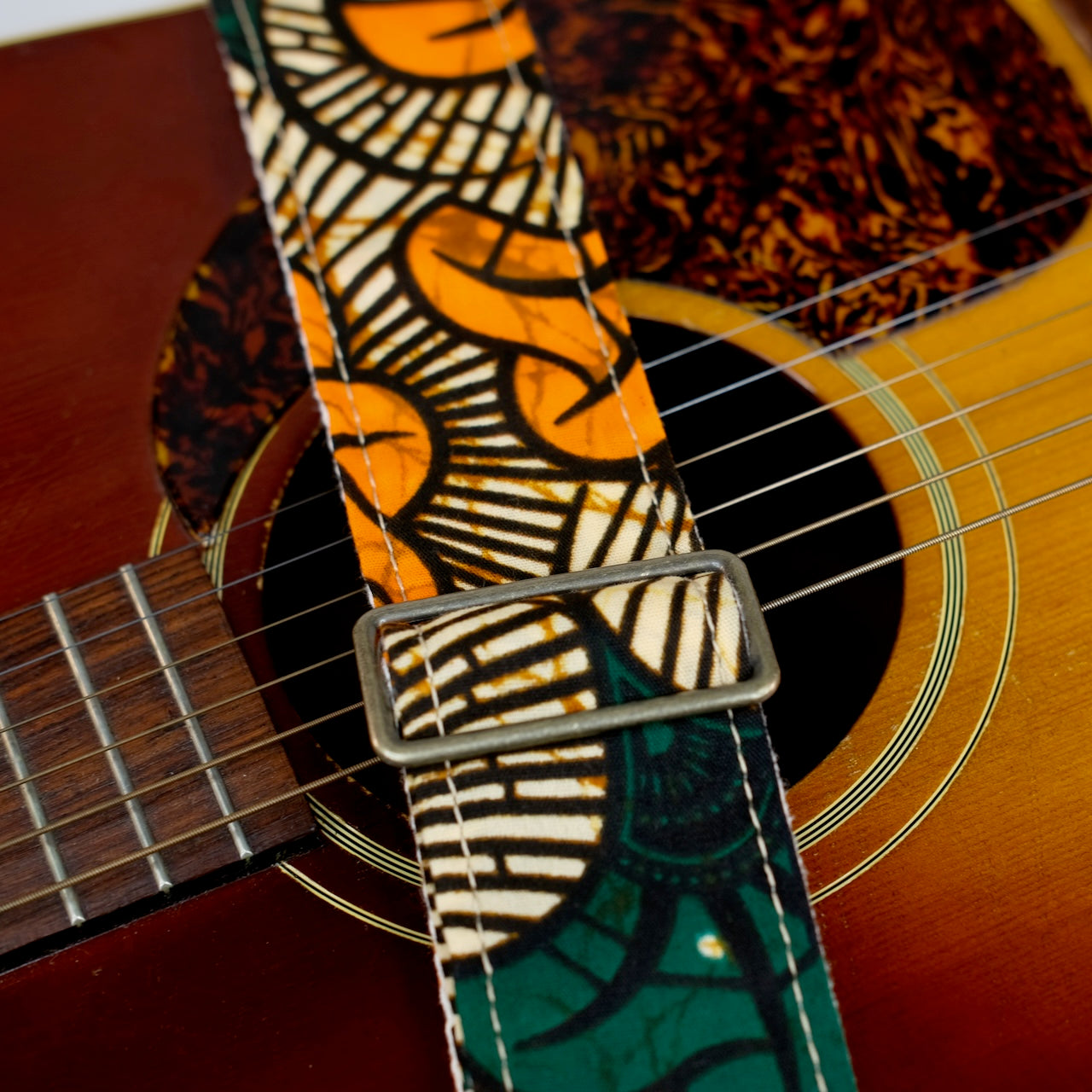 Buckle detail of guitar strap in tan, orange, and green botanical African wax print fabric with brown leather end-tab. Made in Nashville by Original Fuzz.