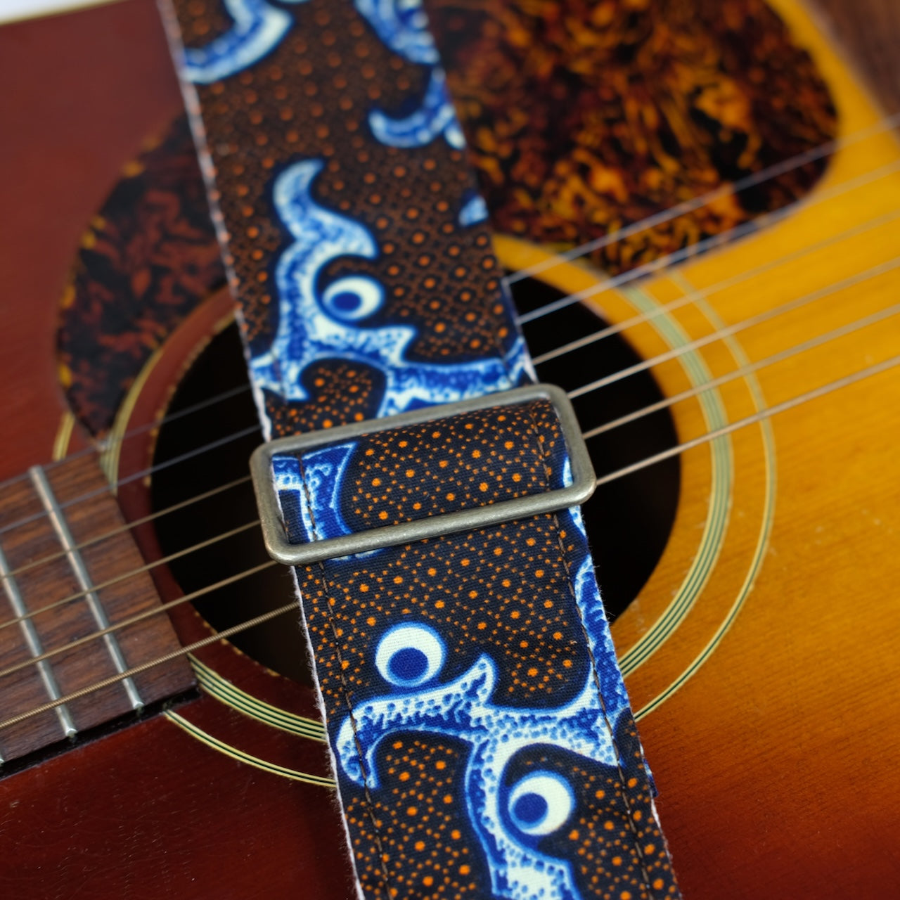 Buckle detail of guitar strap in black, blue, cream, and orange botanical African wax print fabric with black leather end-tab. Made in Nashville by Original Fuzz.
