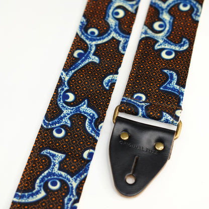End-tab detail view of guitar strap in black, blue, cream, and orange botanical African wax print fabric with black leather end-tab. Made in Nashville by Original Fuzz.