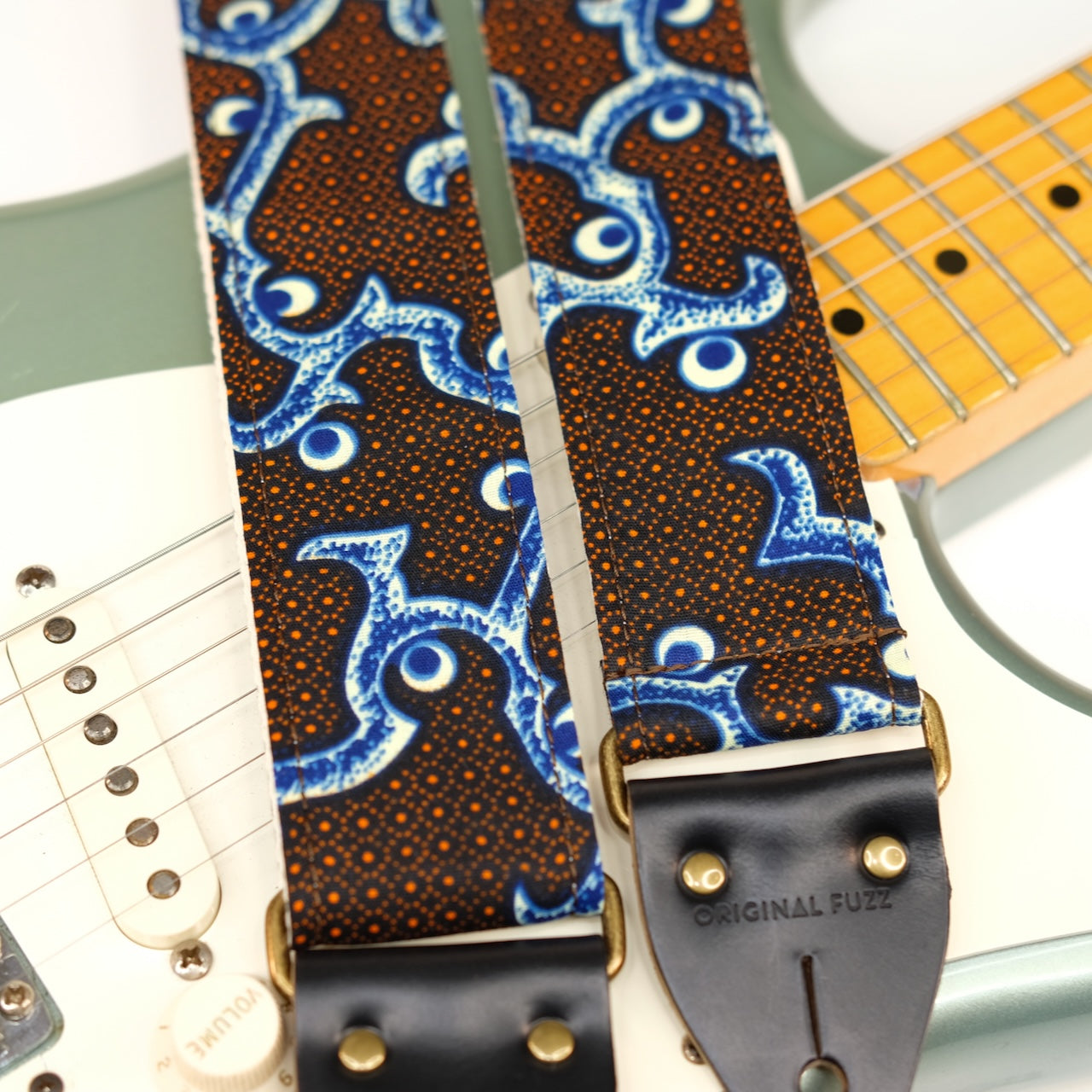 Wide view of guitar strap in black, blue, cream, and orange botanical African wax print fabric with black leather end-tab. Made in Nashville by Original Fuzz.