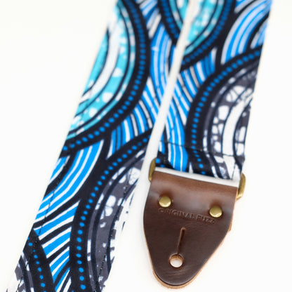 End-tab detail view of guitar strap in teal, gray, white, black, and blue rippled African wax print fabric with brown leather end-tab. Made in Nashville by Original Fuzz.