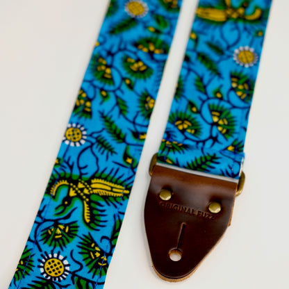 End-tab detail view of guitar strap in blue, yellow, and green botanical African wax print fabric with brown leather end-tab. Made in Nashville by Original Fuzz.