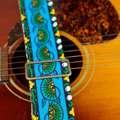 Buckle detail of guitar strap in blue, yellow, and green bordered botanical African wax print fabric with brown leather end-tab. Made in Nashville by Original Fuzz.