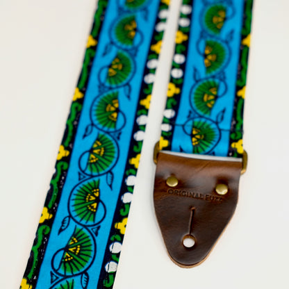 End-tab detail view of guitar strap in blue, yellow, and green bordered botanical African wax print fabric with brown leather end-tab. Made in Nashville by Original Fuzz.
