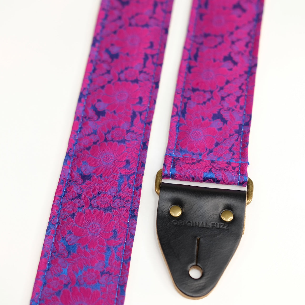 End-tab detail view of guitar strap in pink and blue silk floral fabric with black leather end-tab. Made in Nashville by Original Fuzz.