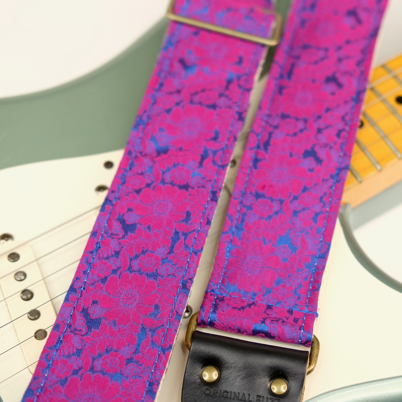 Wide view of guitar strap in pink and blue silk floral fabric with black leather end-tab. Made in Nashville by Original Fuzz.