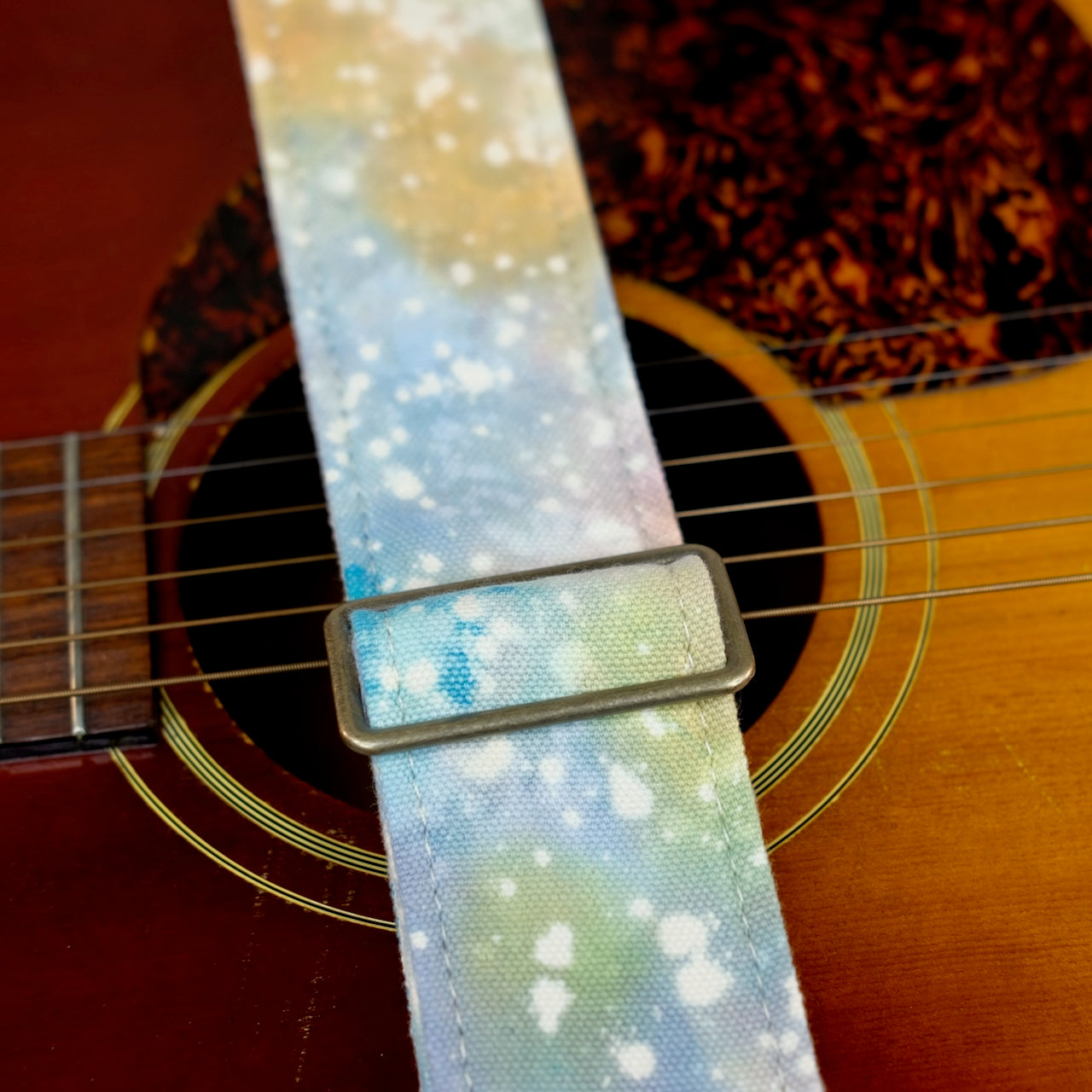 Buckle detail of guitar strap in multi-colored over cream base hand-dyed canvas fabric with brown leather end-tab. Made in Nashville by Original Fuzz.