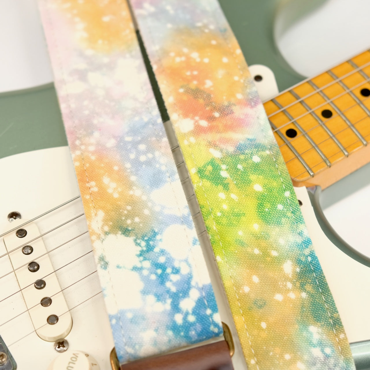 Wide view of guitar strap in multi-colored over cream base hand-dyed canvas fabric with brown leather end-tab. Made in Nashville by Original Fuzz.