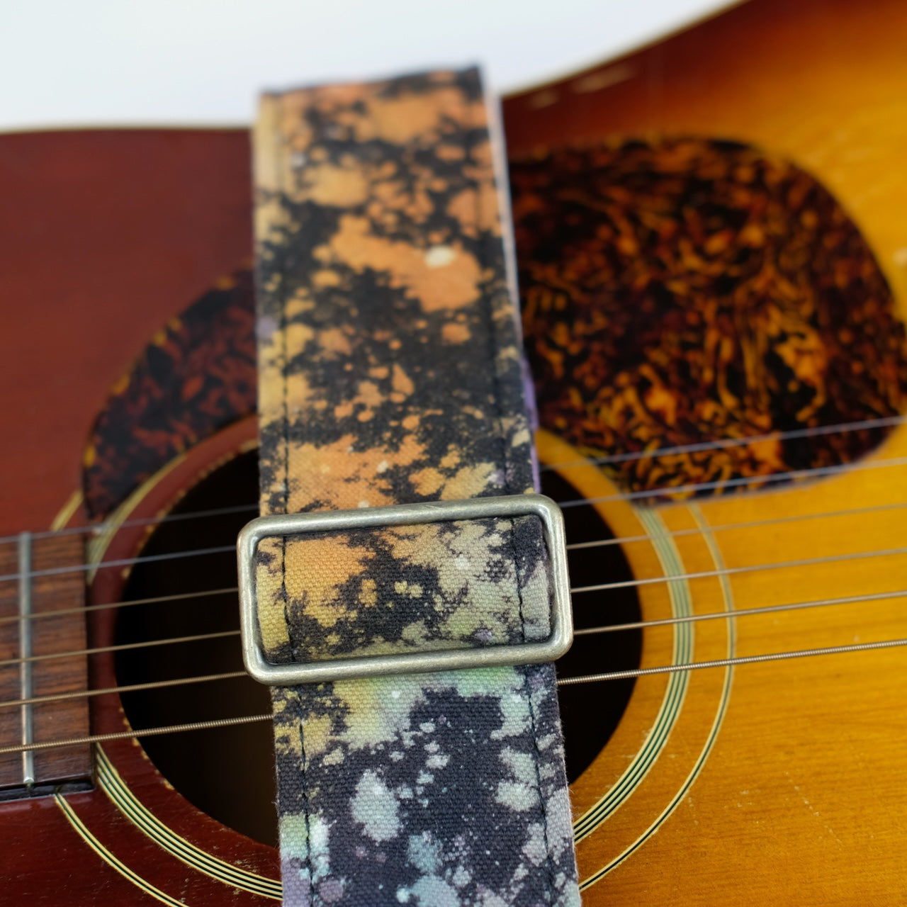 Buckle detail of guitar strap in multi-colored over black base hand-dyed canvas fabric with black leather end-tab. Made in Nashville by Original Fuzz.