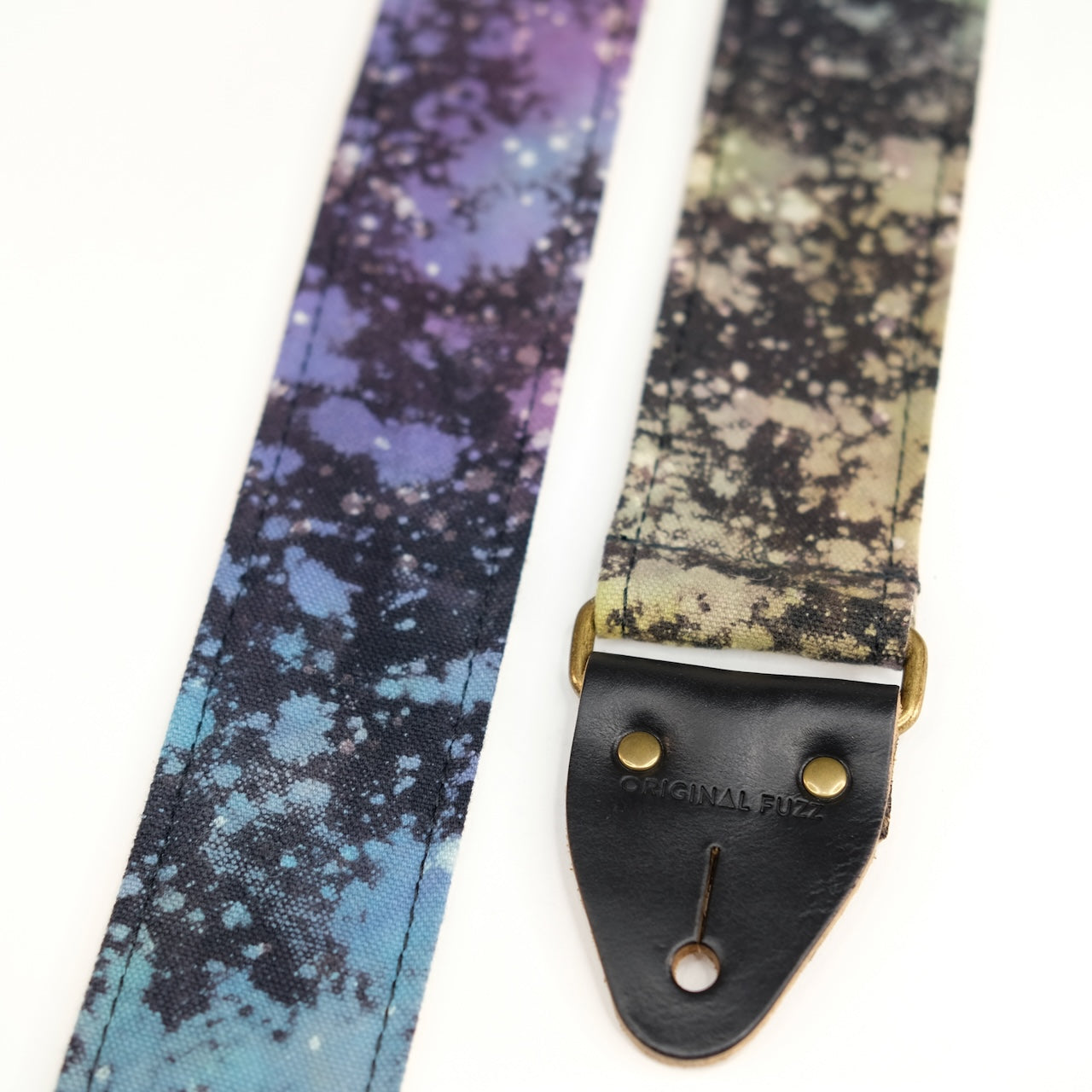 End-tab detail view of guitar strap in multi-colored over black base hand-dyed canvas fabric with black leather end-tab. Made in Nashville by Original Fuzz.