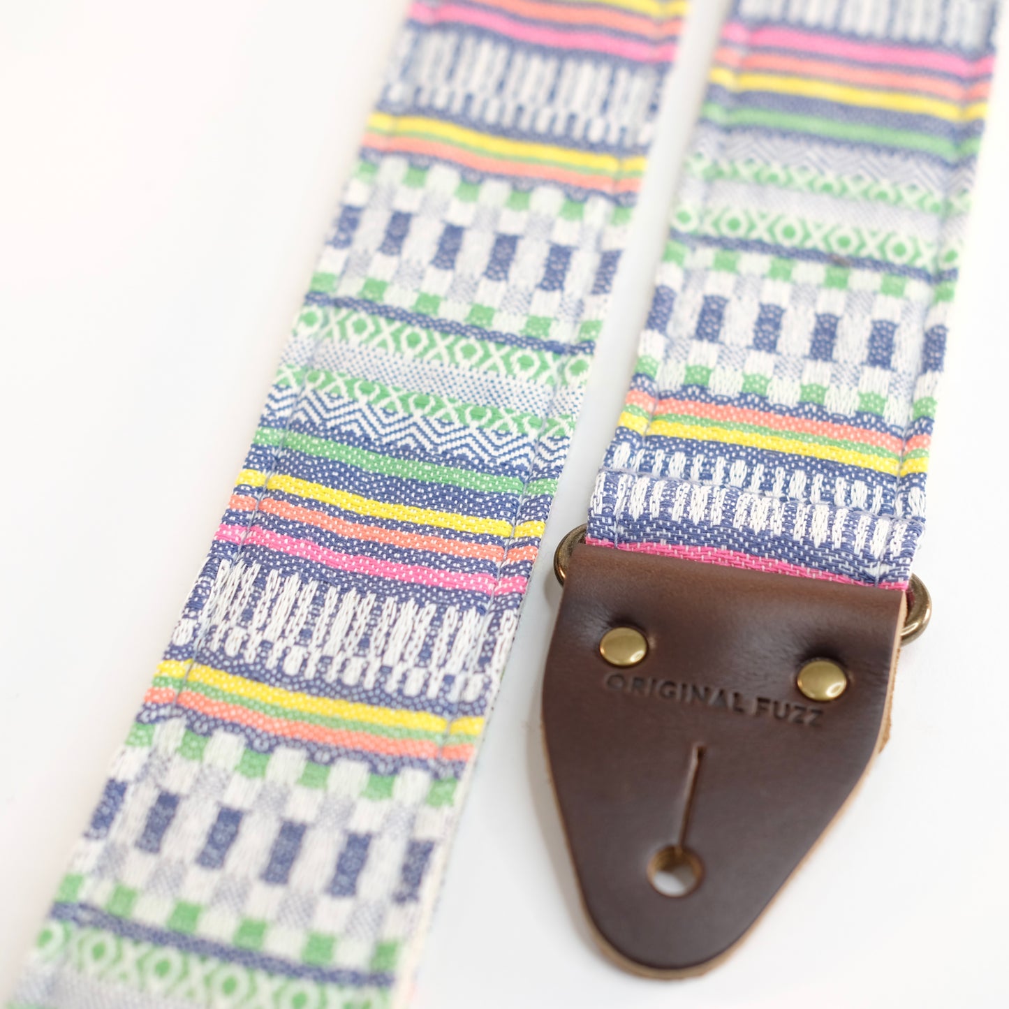 End-tab detail view of guitar strap in white, blue, and green geometric woven fabric with brown leather end-tab. Made in Nashville by Original Fuzz.