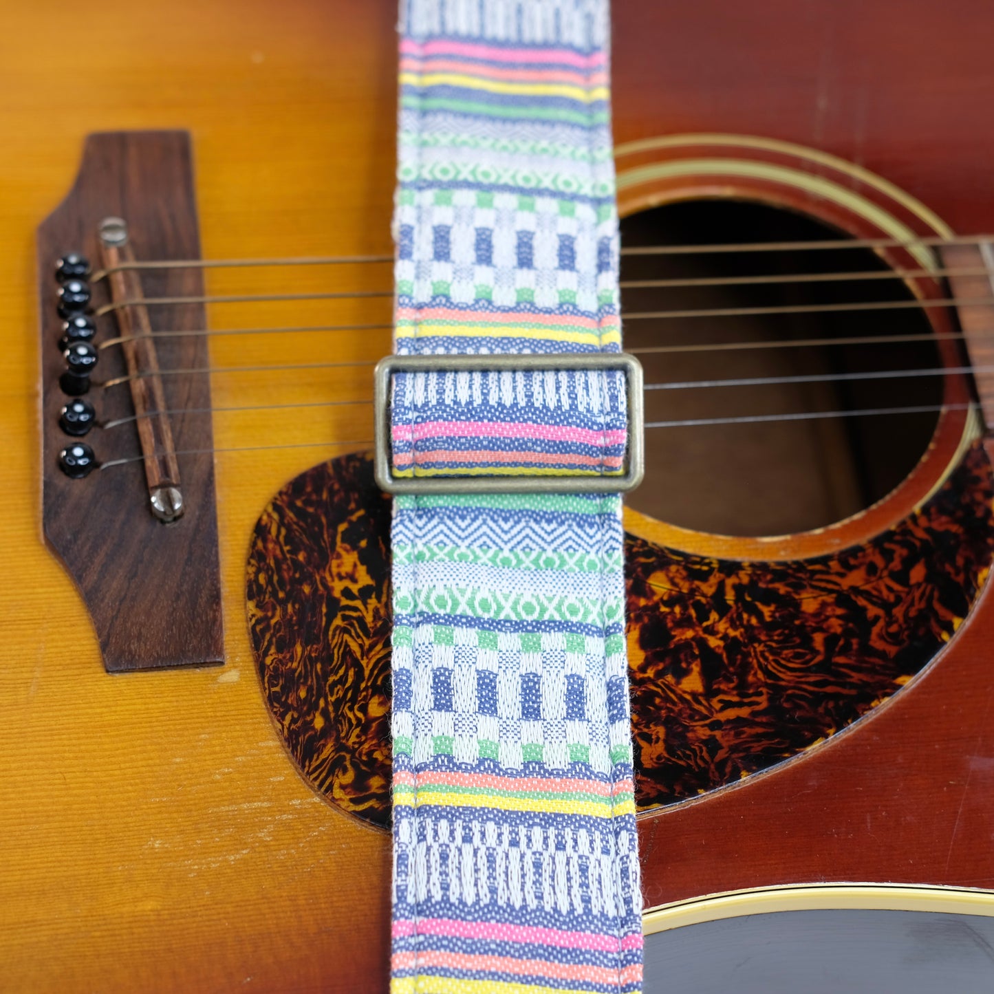 Buckle detail of guitar strap in white, blue, and green geometric woven fabric with brown leather end-tab. Made in Nashville by Original Fuzz.