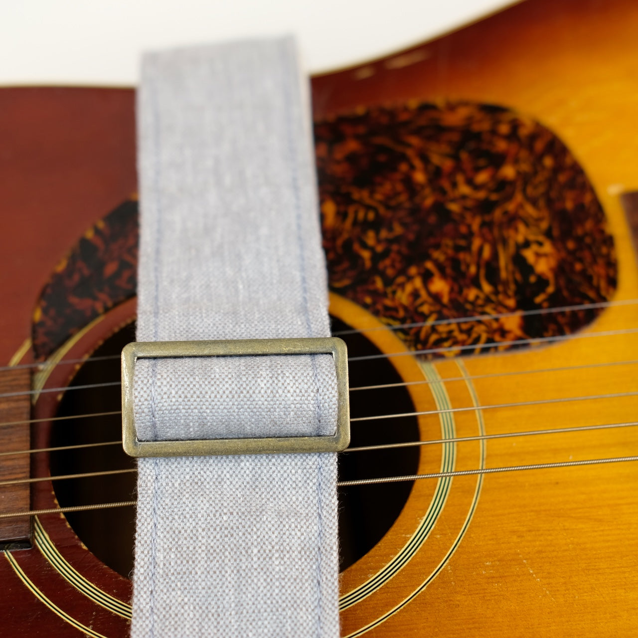 Buckle detail of guitar strap in cool light grey shimmery woven fabric with brown leather end-tab. Made in Nashville by Original Fuzz.