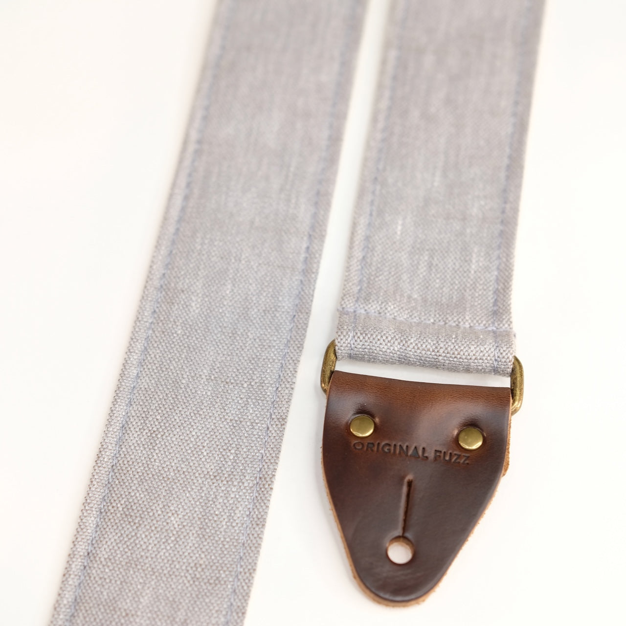 End-tab detail view of guitar strap in cool light grey shimmery woven fabric with brown leather end-tab. Made in Nashville by Original Fuzz.