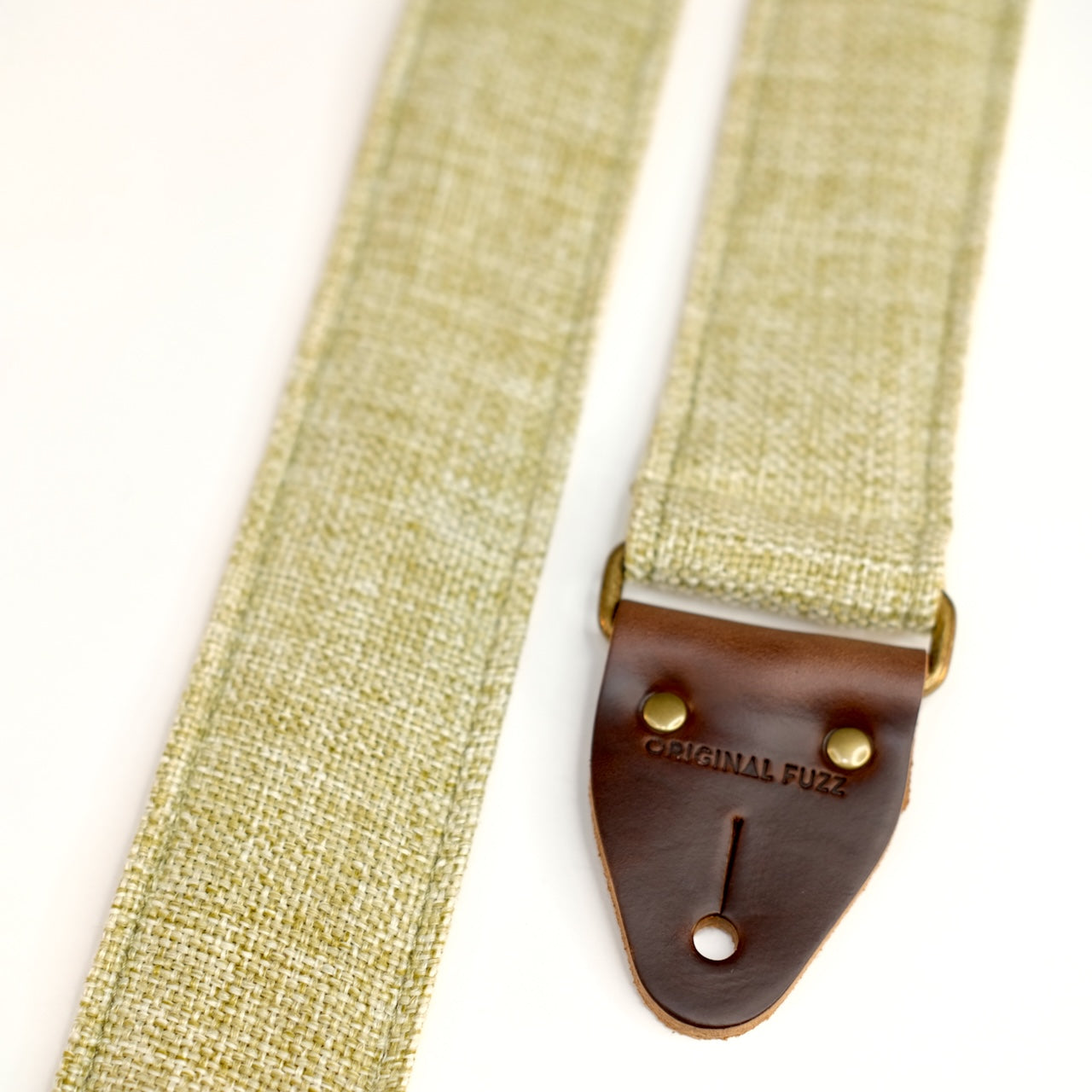 End-tab detail view of guitar strap in green and cream woven fabric with brown leather end-tab. Made in Nashville by Original Fuzz.