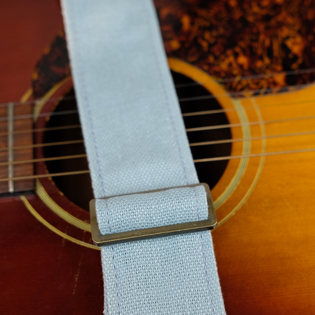 Buckle detail of guitar strap in light blue woven fabric with brown leather end-tab. Made in Nashville by Original Fuzz.