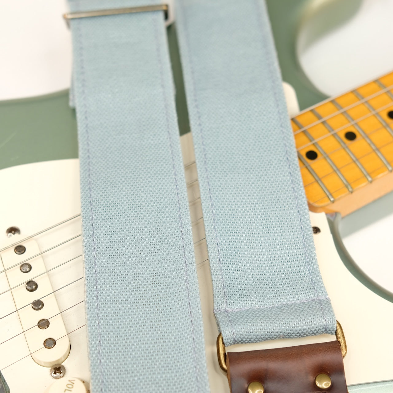 Wide view of guitar strap in light blue woven fabric with brown leather end-tab. Made in Nashville by Original Fuzz.