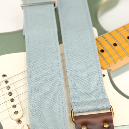 Wide view of guitar strap in light blue woven fabric with brown leather end-tab. Made in Nashville by Original Fuzz.